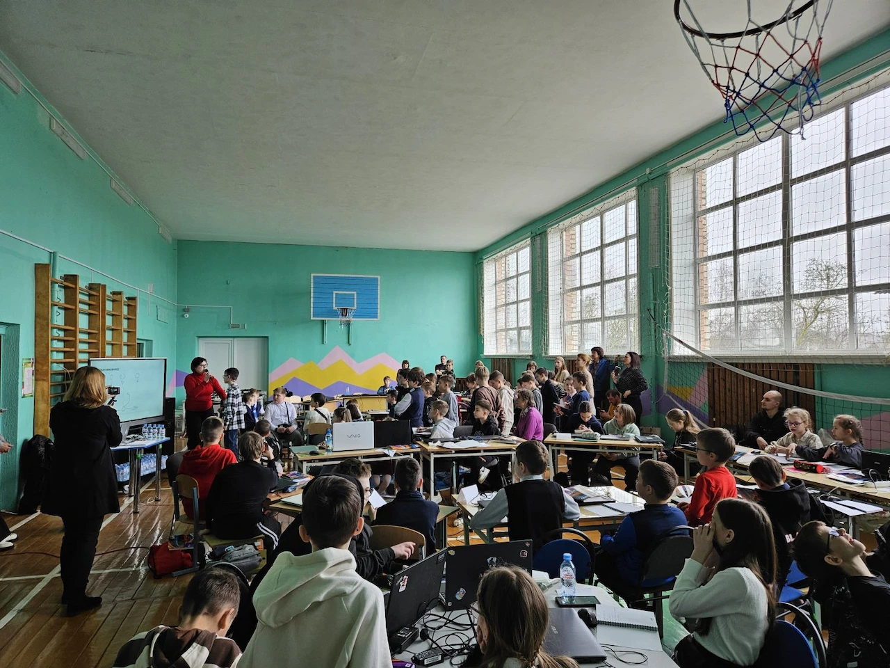 https://unificont-web-assets-production.mntprod.net/assets/lesta-games-start/Школьники в спортивном зале слушают учителя